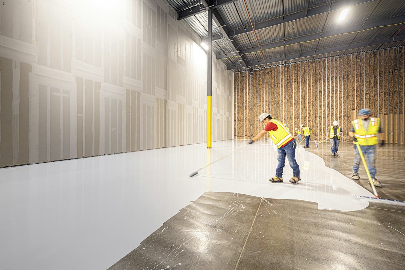 Workers spreading white floor coating in an industrial space