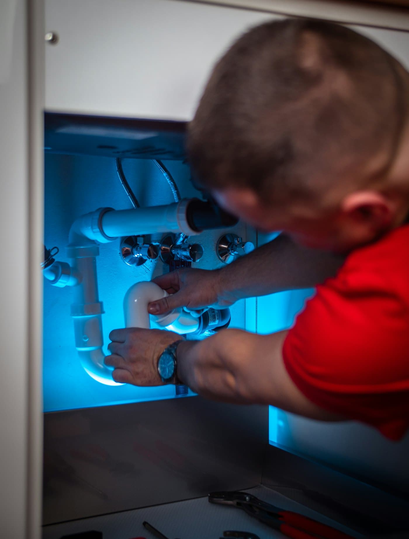 Plumber repairing the waste pipe under a sink