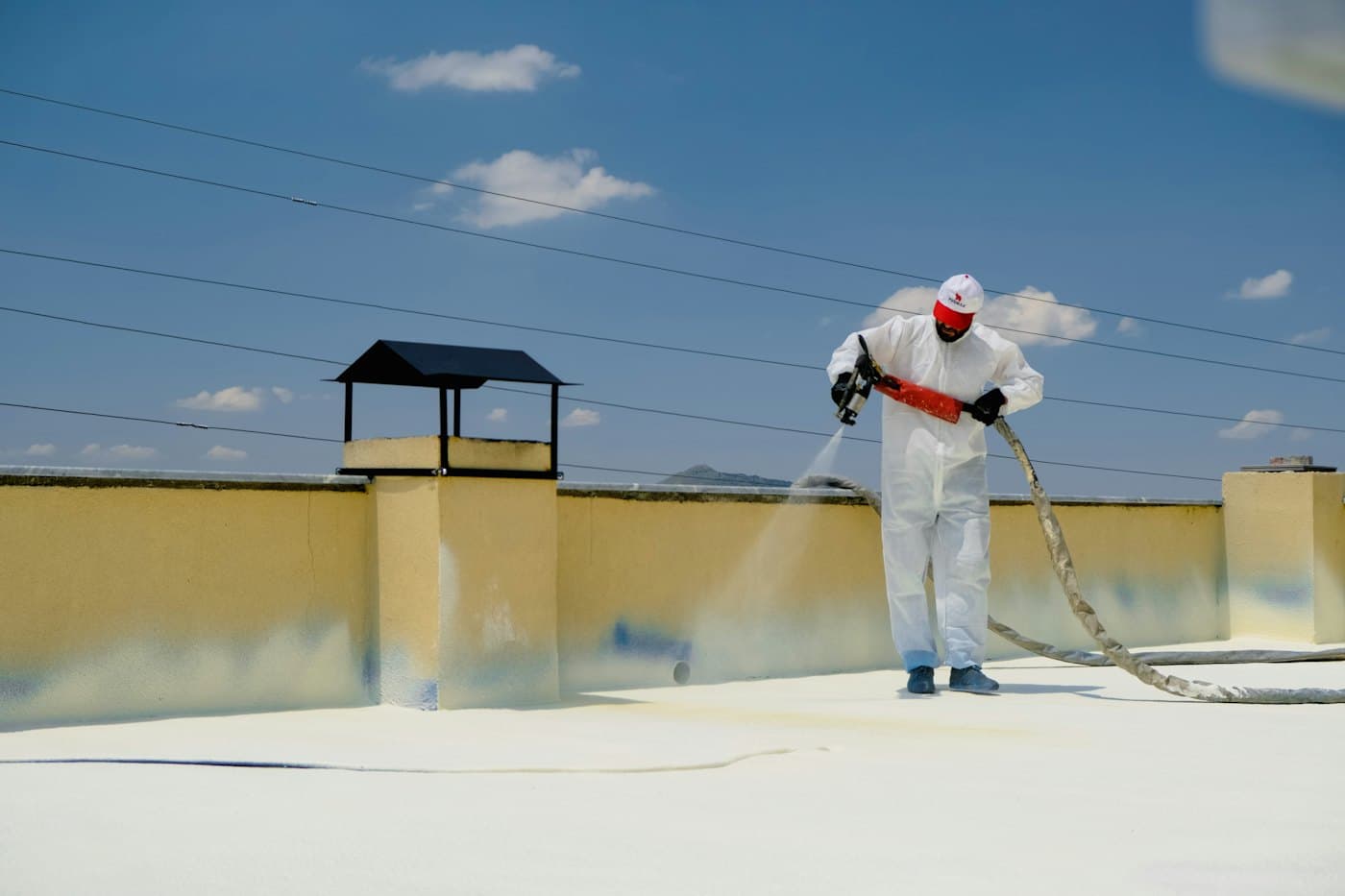 Worker in protective suit spraying a waterproof coating on a roof